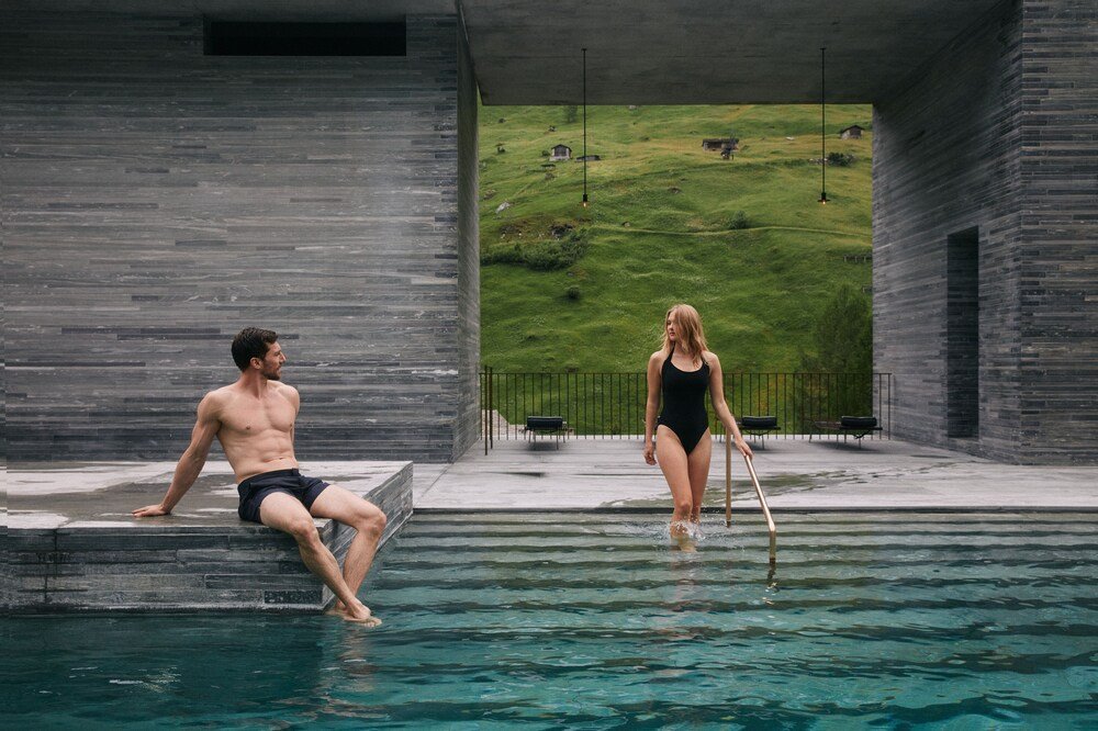 Hombre y mujer junto a una piscina con vista a una ladera verde