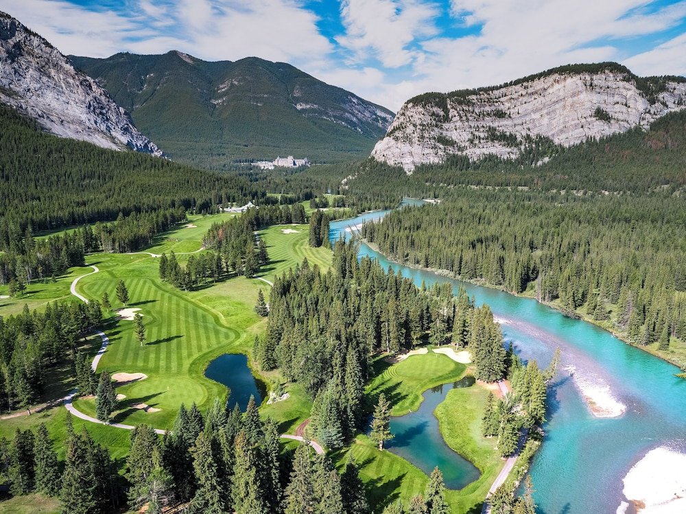 Golf course beside a river, surrounded by forest and mountains