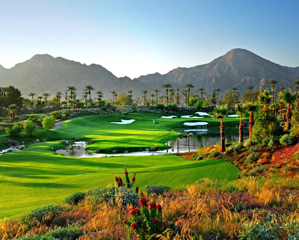 Campo de golf con un estanque, palmeras y montañas al fondo